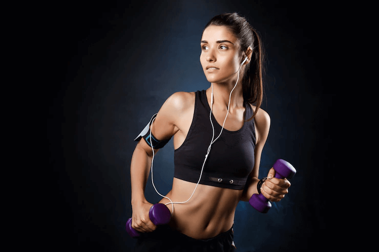 Girl training in ports bra with dumbbells over a dark wall