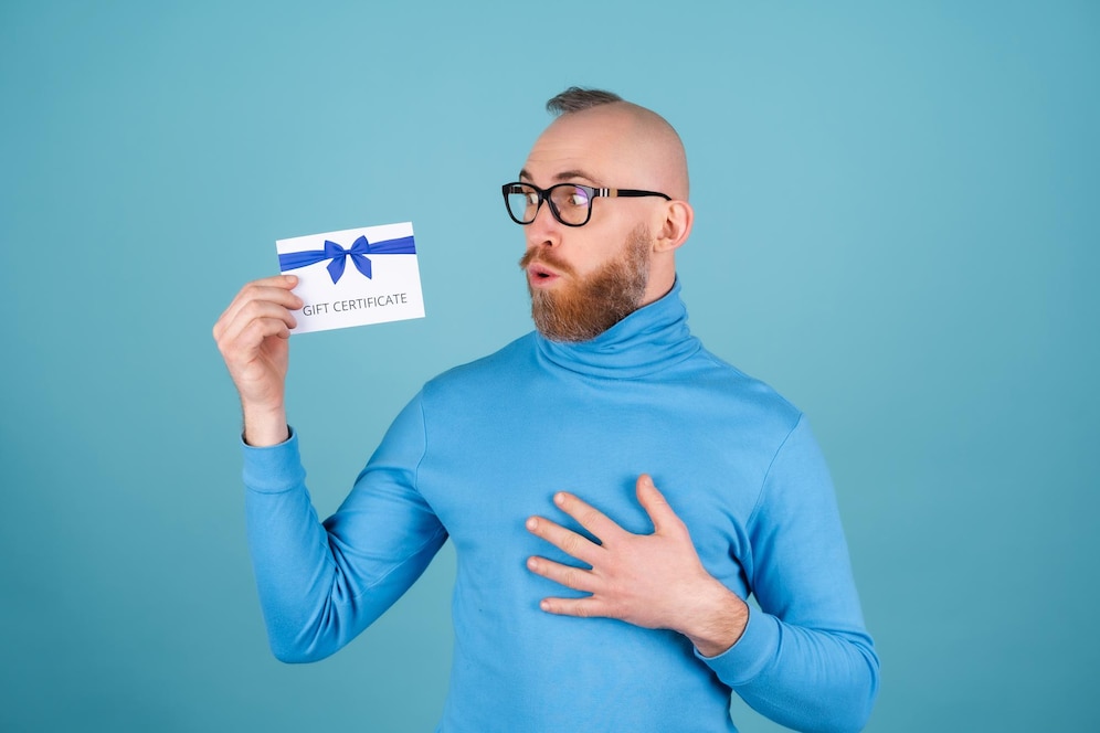 A young man on a blue background holds a gift certificate