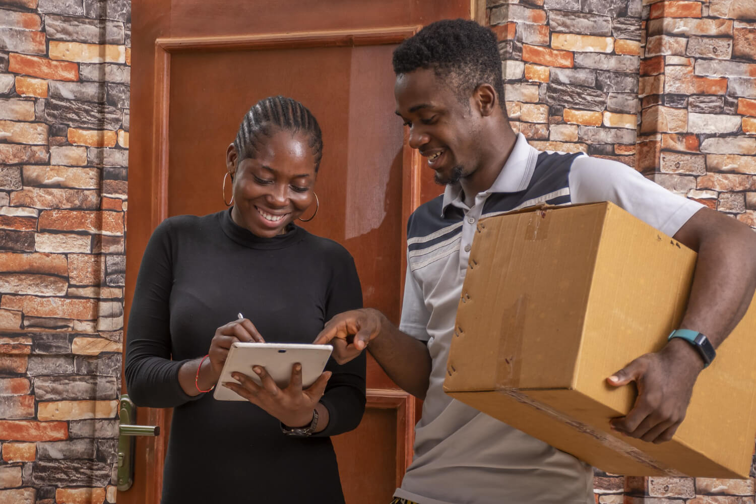 Smiling woman receiving a package from a man and signing a proof of delivery