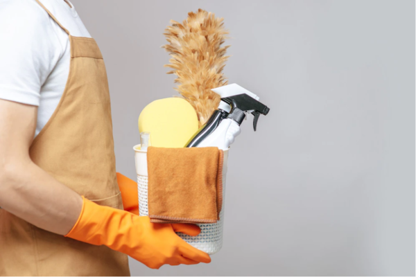 close up hand of a young man in an apron and rubber gloves holding a basket of cleaning equipment